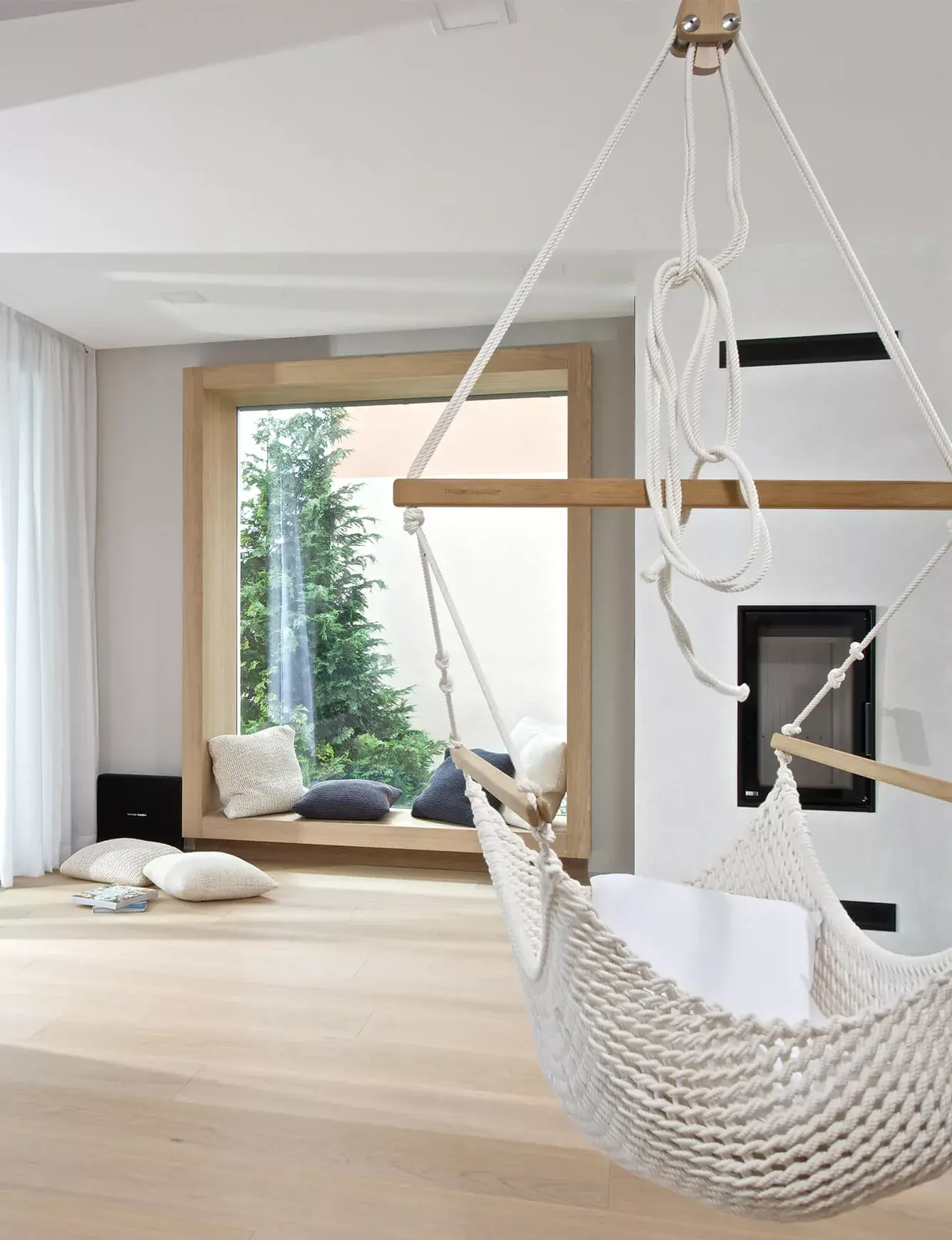 Prosvětlený interiér obývacího pokoje v soukromém domě na Moravě, kde k relaxační atmosféře přispívá světlá dubová podlaha Oakcent Rustic v odstínu Light White, doplněná o designovou závěsnou houpací síť a útulné okenní posezení s výhledem do zahrady.