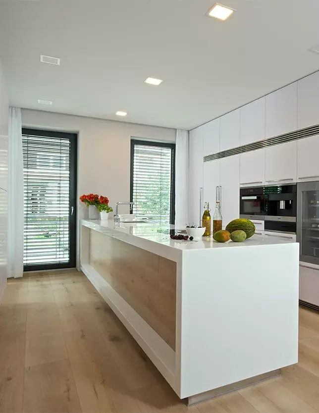 Detailní pohled na bílý kuchyňský ostrůvek s bočním obložením z dubového dřeva, který barevně i strukturou plynule navazuje na široká dubová prkna podlahy Oakcent Rustic v odstínu Light White.