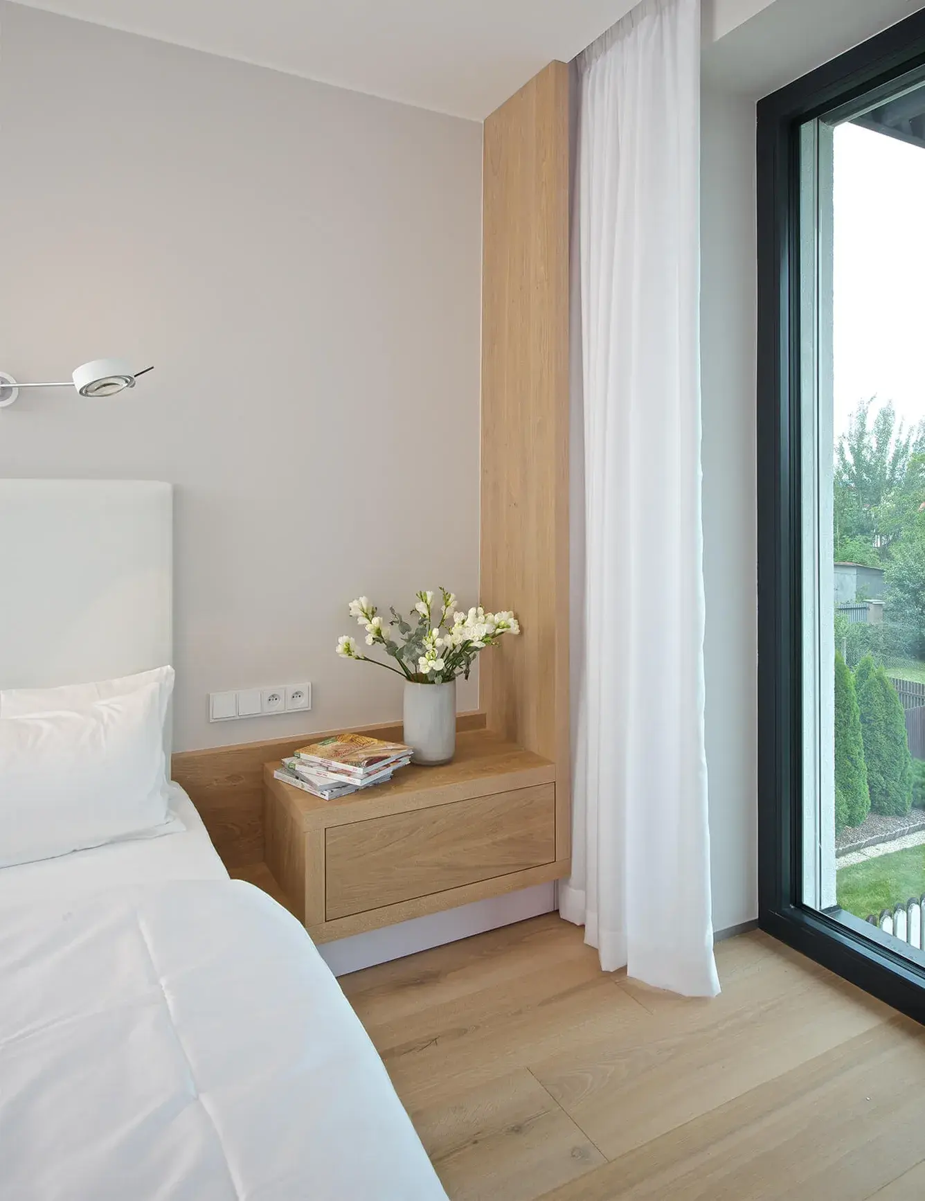 Detailní pohled na minimalistický noční stolek a čelo postele z dubového dřeva v ložnici moravského domu, které barevně ladí s podlahou Oakcent Rustic v odstínu Light White a vytváří klidnou atmosféru pro odpočinek.