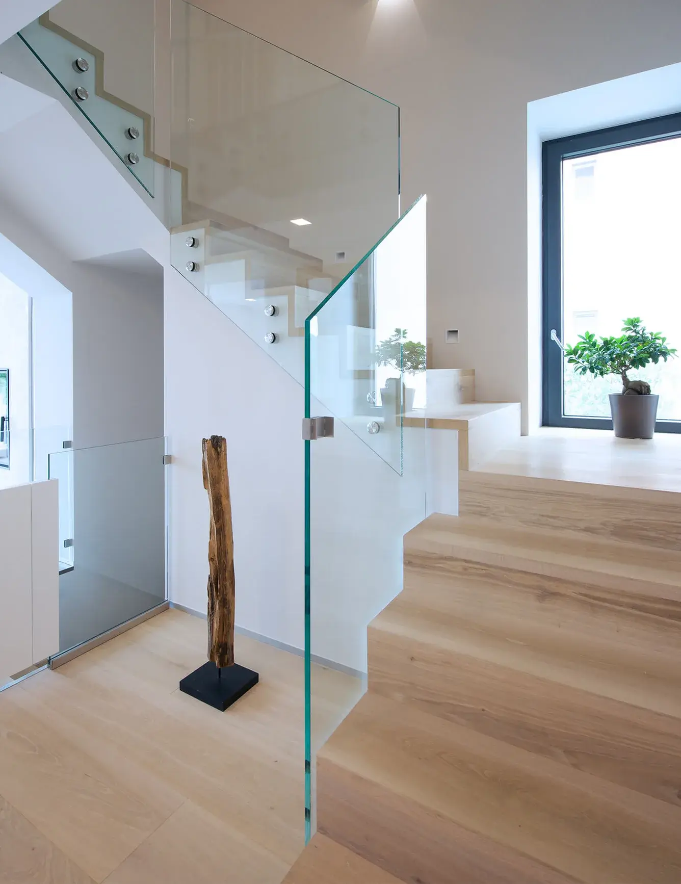 Detailní pohled na moderní schodiště v soukromém domě na Moravě, kde jsou stupně i navazující podlaha realizovány z dubových prken Oakcent Rustic v odstínu Light White, doplněné o minimalistické skleněné zábradlí.