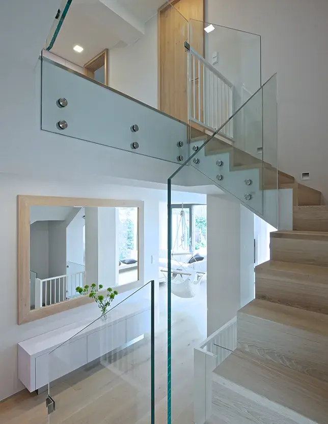 Široký pohled na prosvětlené schodiště v soukromém domě na Moravě, kde jsou nášlapy i navazující podlaha realizovány z dubových prken Oakcent Rustic v odstínu Light White, doplněné o moderní skleněné zábradlí s nerezovými úchyty.