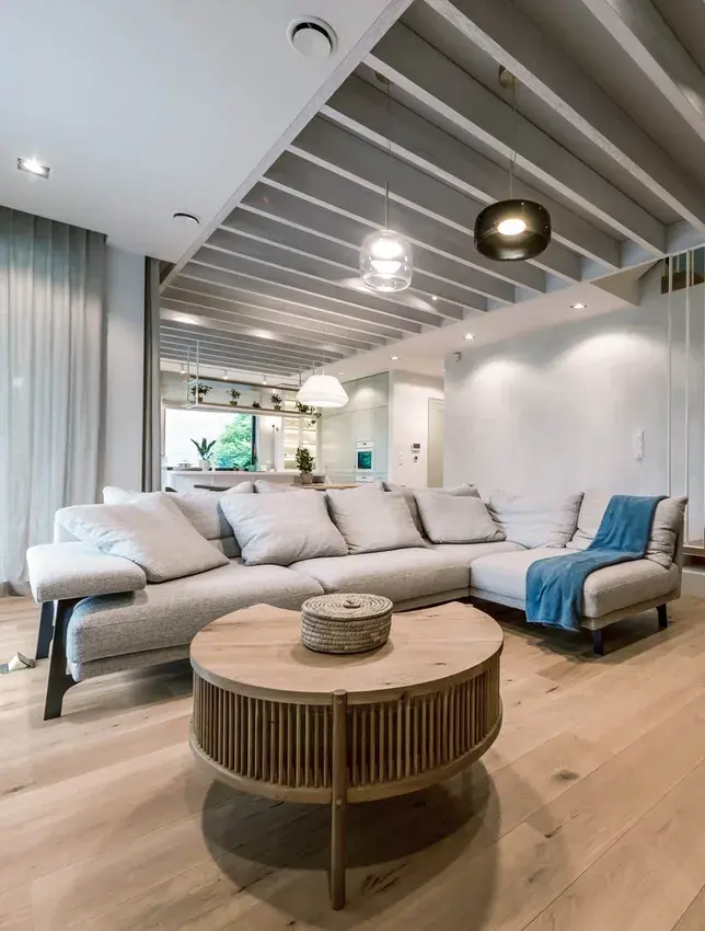 Detail obývacího pokoje v krakovském domě Motyla se zaměřením na kouřovanou dubovou podlahu Oakcent Rustic v přírodním odstínu Pure, jejíž masivní prkna ve formátu $195/2200$ mm doplňují moderní lamelový podhled a světlou sedací soupravu.