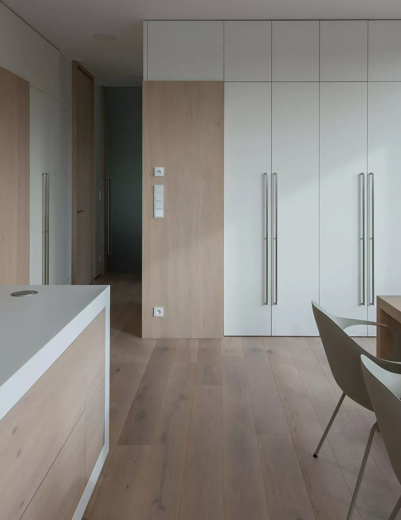 Detailní pohled na minimalistickou šatní stěnu v pražském střešním bytě od ID_arch, kde bílé hladké plochy s dlouhými nerezovými madly doplňuje dubový dekor vestaveb a lehce kouřovaná dubová podlaha Oakcent Rustic pod Milky olejem.