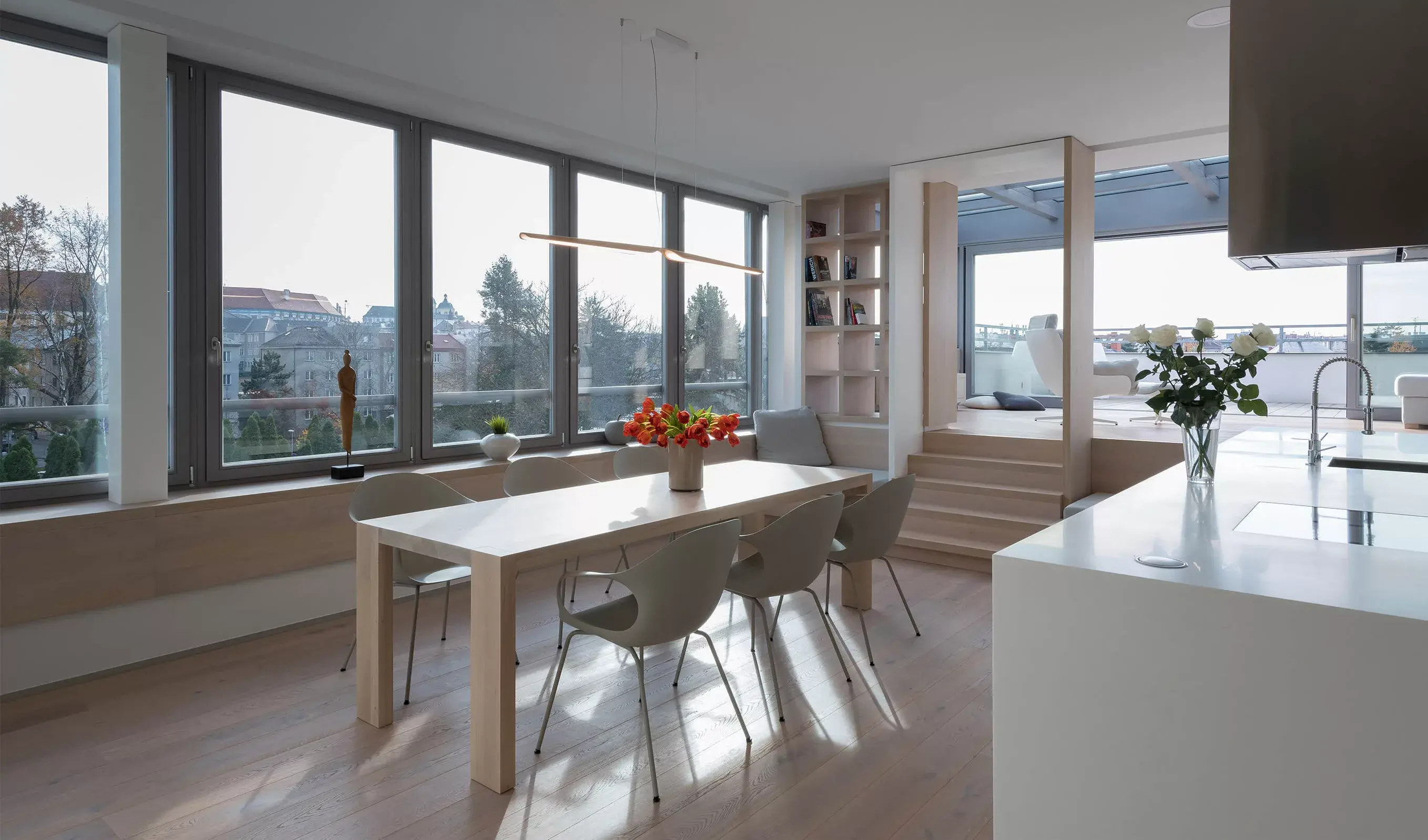 Panoramatický pohled na jídelní kout pražského střešního bytu od ID_arch, kde kartáčovaná dubová podlaha Oakcent v odstínu Milky tvoří jednotný základ pro světlý interiér s velkorysými prosklenými plochami a výhledem na město.