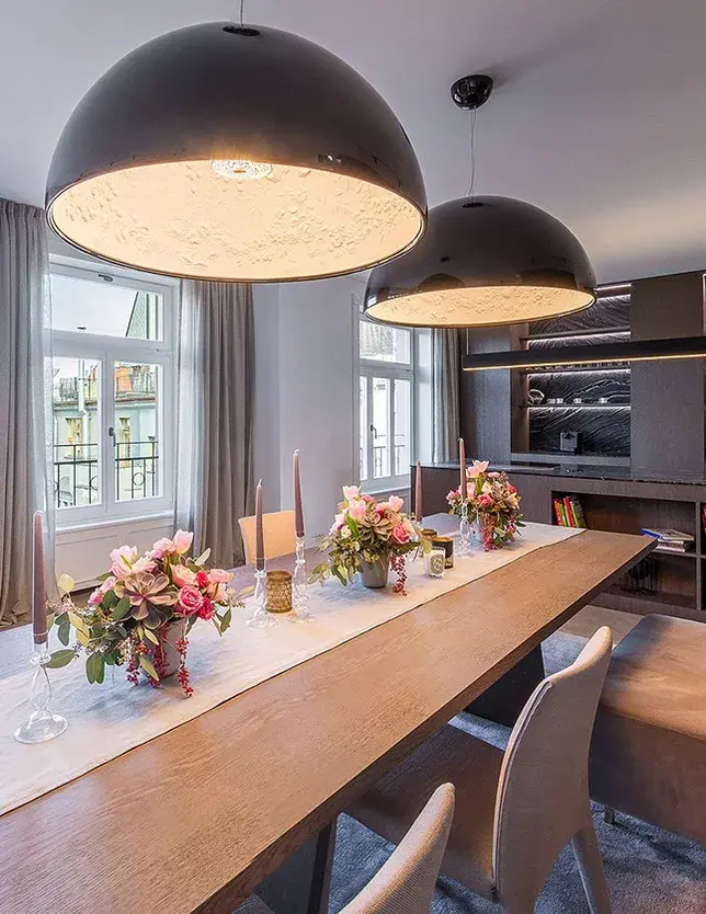 Detailní záběr na prostřený jídelní stůl v reprezentativním staroměstském apartmánu, kterému dominují dvě velká černá polokulovitá svítidla a šedá dubová podlaha Oakcent Smoke Herringbone v pozadí.