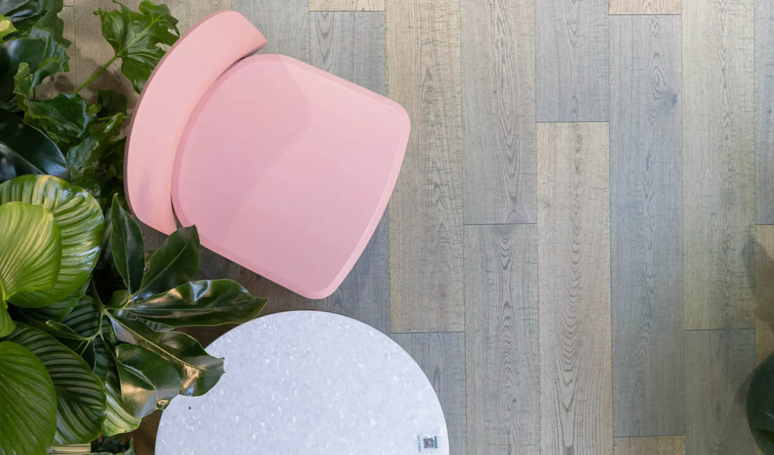 Alt text: Pohled z ptačí perspektivy na detail interiéru Healthy Longevity Café, kde růžová židle a kulatý stolek s terazzo vzorem kontrastují s vícebarevnou dubovou podlahou Oakcent vyskládanou z lamel různých odstínů.