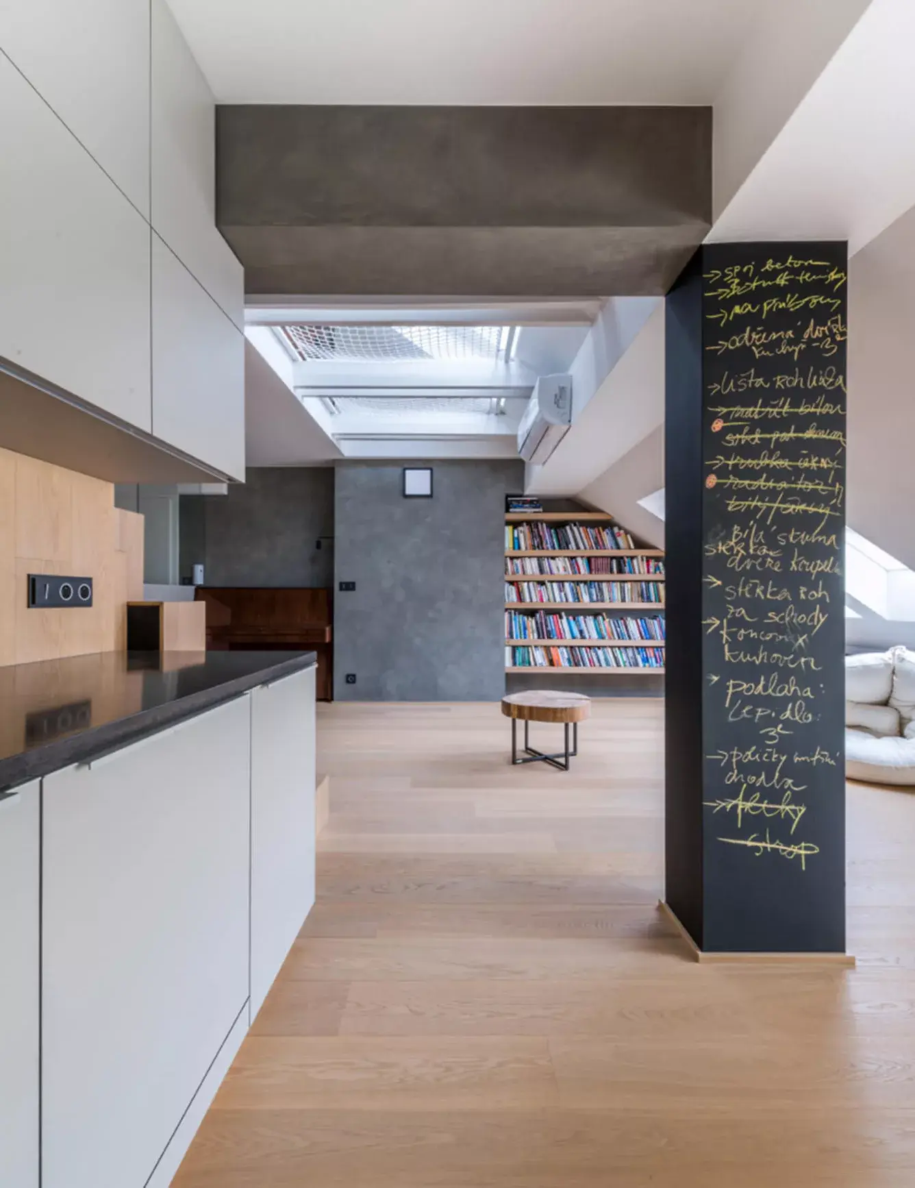 Prosvětlený interiér podkrovního bytu Karlínské útočiště s dubovou podlahou a vestavěnou knihovnou, který studio Vladan Běhal Design přetvořilo z dispozice 4+kk na velkorysý otevřený prostor 2+kk.