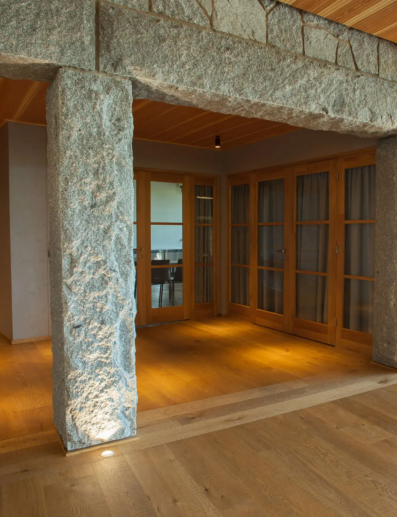 Rustikální dubová podlaha v interiéru Panorama Golf Resortu v Kácově, kde přírodní dřevo kontrastuje s masivními kamennými pilíři a dřevěnými prosklenými dveřmi v návrhu architektů Martina Rajniše a Mojmíra Ranného.