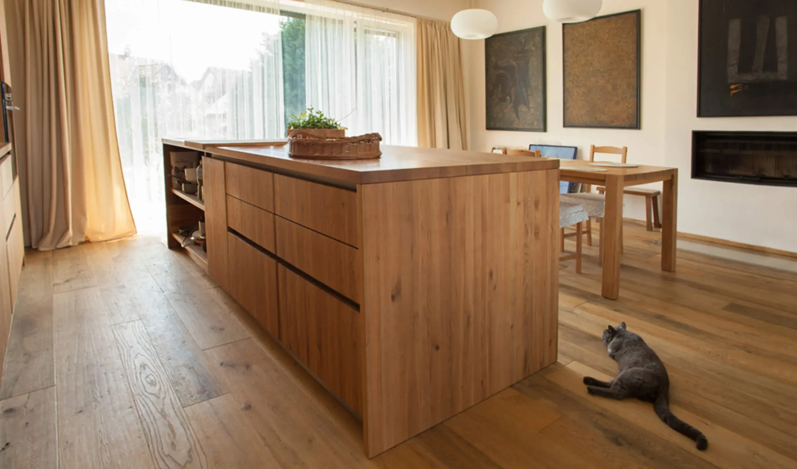 Široký pohled do prosvětleného obývacího prostoru s kuchyňským koutem v Uherském Hradišti, kde dubová podlaha Oakcent Rustic s nano olejem a běleným louhovaným povrchem tvoří hřejivý základ pro masivní dřevěný ostrůvek, u kterého odpočívá kočka.