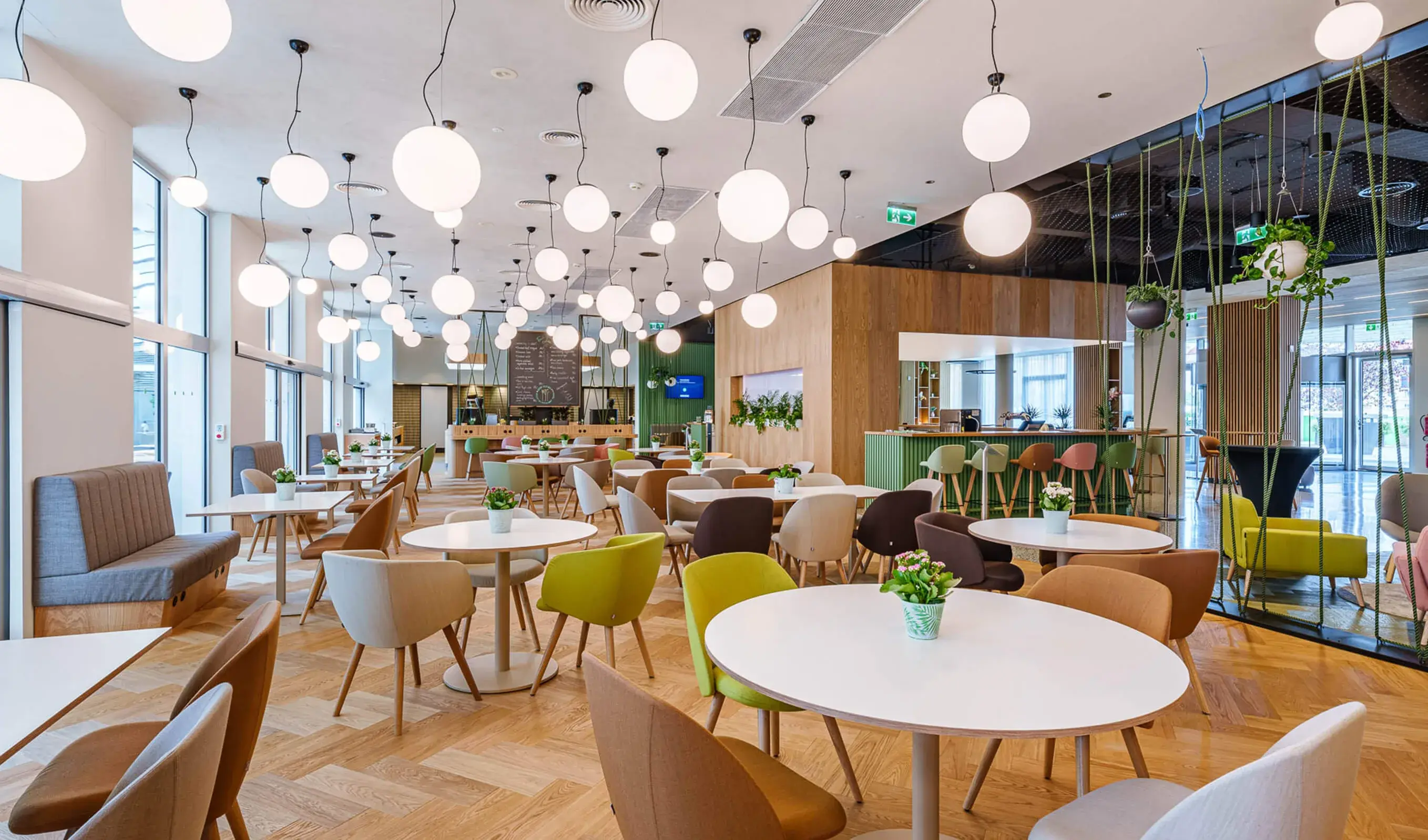 Pohled do moderního lobby hotelu Holiday Inn v Praze, kterému dominuje prosvětlený zvlněný podhled a dřevěná stěna s vinotékou, doplněná o barevná křesílka a dubovou podlahu Oakcent ve vzoru rybí kost.