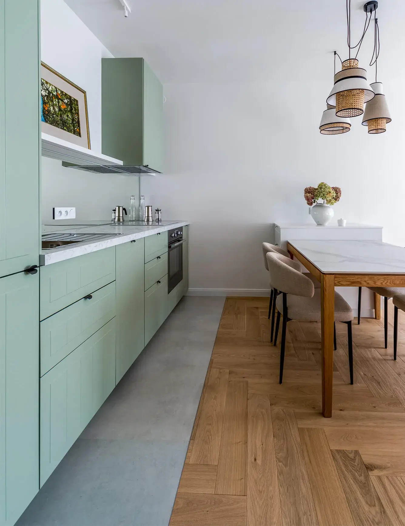 Moderní kuchyně s jídelním koutem v mini apartmánu ve Varšavě, kde mátově zelená kuchyňská linka plynule přechází z šedé dlažby na dubovou podlahu Oakcent Rustic položenou ve vzoru stromečku (Herringbone).