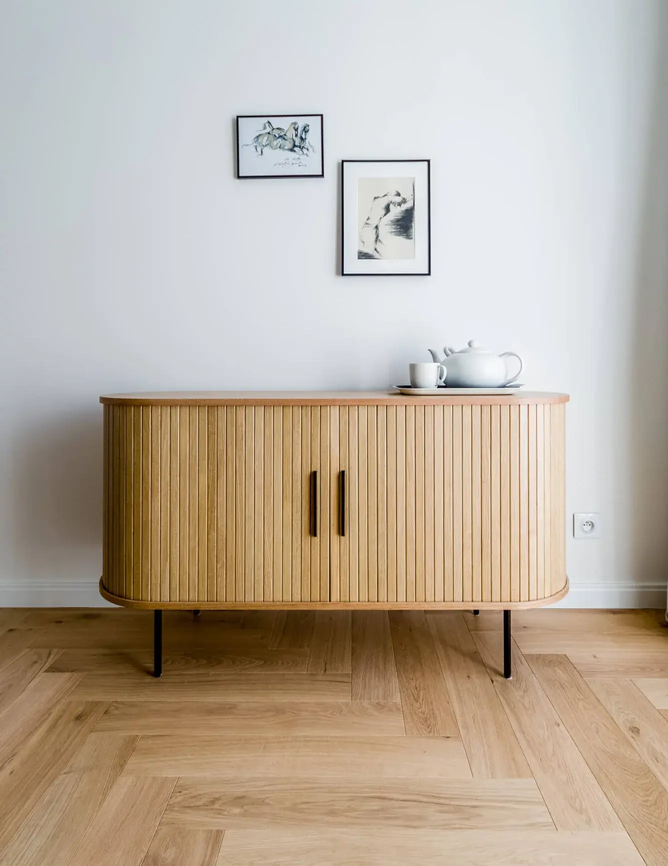 Detailní čelní pohled na designovou dřevěnou komodu se svislým žebrováním v mini apartmánu ve Varšavě, stojící na dubové podlaze Oakcent Rustic položené ve vzoru stromečku (Herringbone).