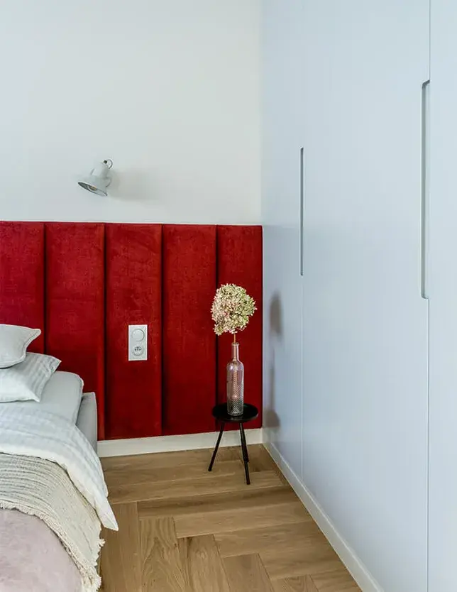 Detailní záběr na ložnici v mini apartmánu ve Varšavě, kterému dominuje postel s výrazným sytě červeným polstrovaným čelem, kontrastujícím se světlou vestavěnou skříní a dubovou podlahou Oakcent Rustic ve vzoru stromečku (Herringbone).