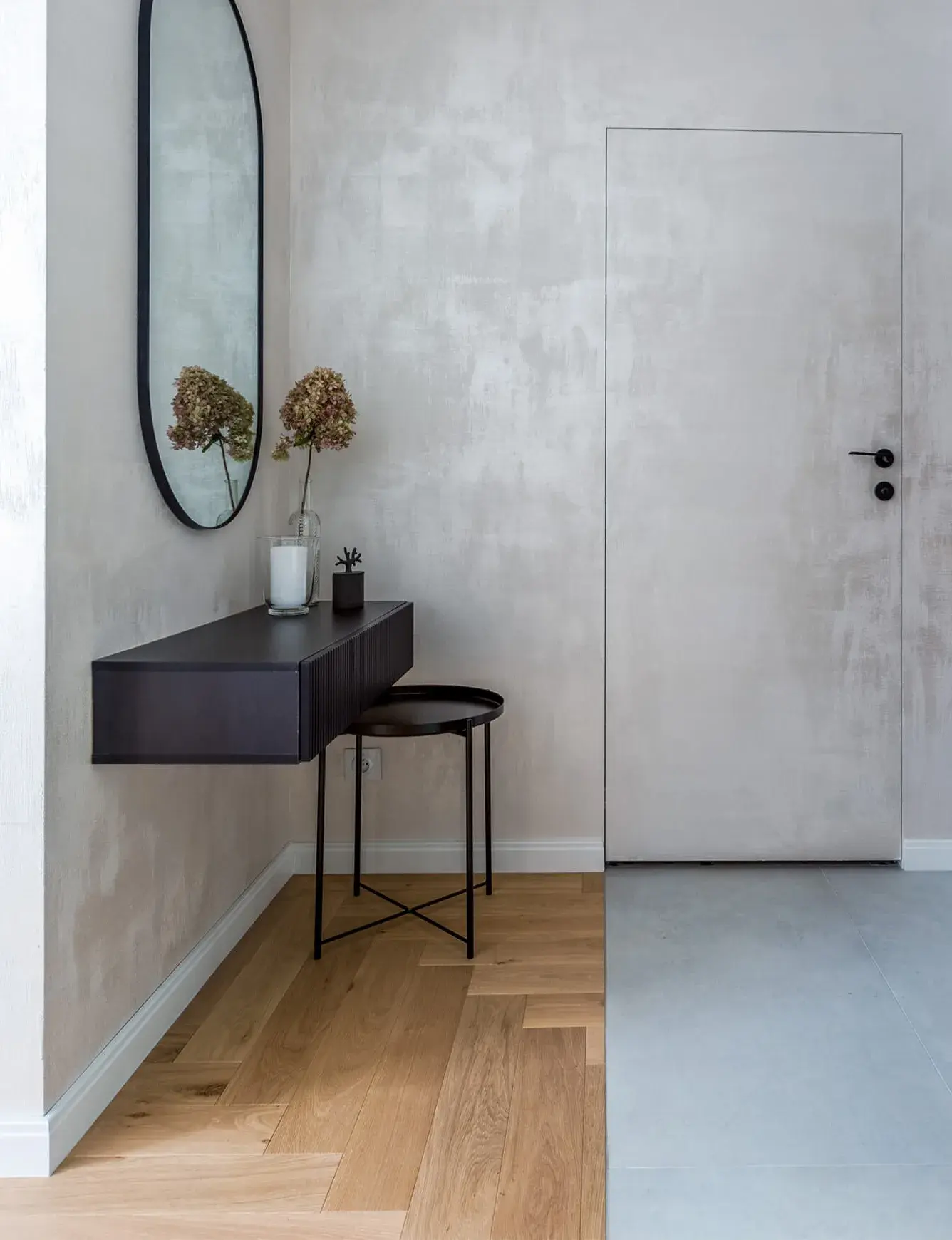 Detailní pohled na přechod materiálů v interiéru mini apartmánu ve Varšavě, kde dubová podlaha Oakcent Rustic položená do vzoru stromečku (Herringbone) navazuje na minimalistickou světle šedou dlažbu u bílých bezfalcových dveří.