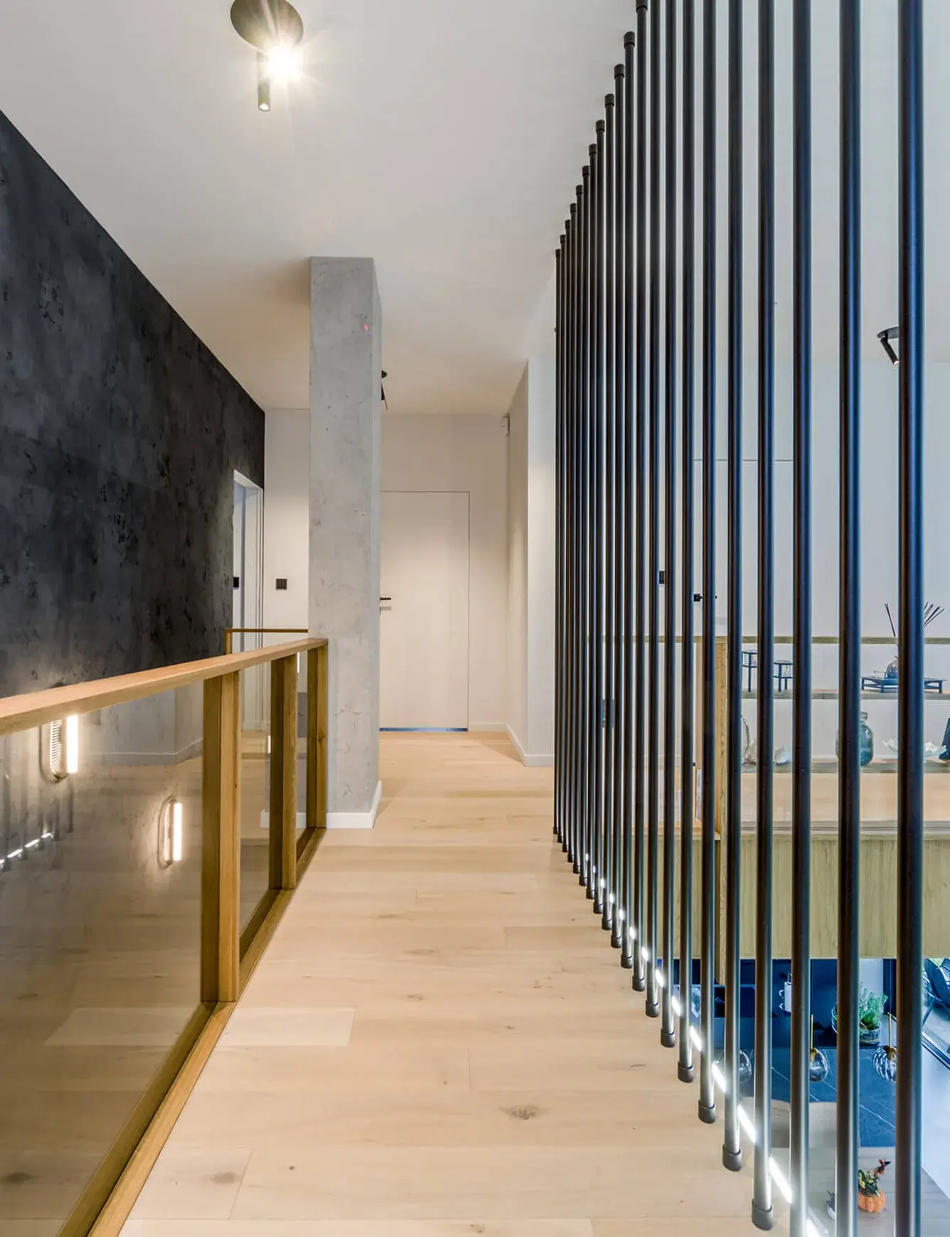 Moderní interiér soukromé rezidence u Vratislavi s dubovou podlahou Oakcent Rustic v dekoru Milky, kterému dominuje minimalistická chodba s industriálními prvky v podobě černé kovové tyčové zástěny a pohledového betonu, doplněná o skleněné zábrad