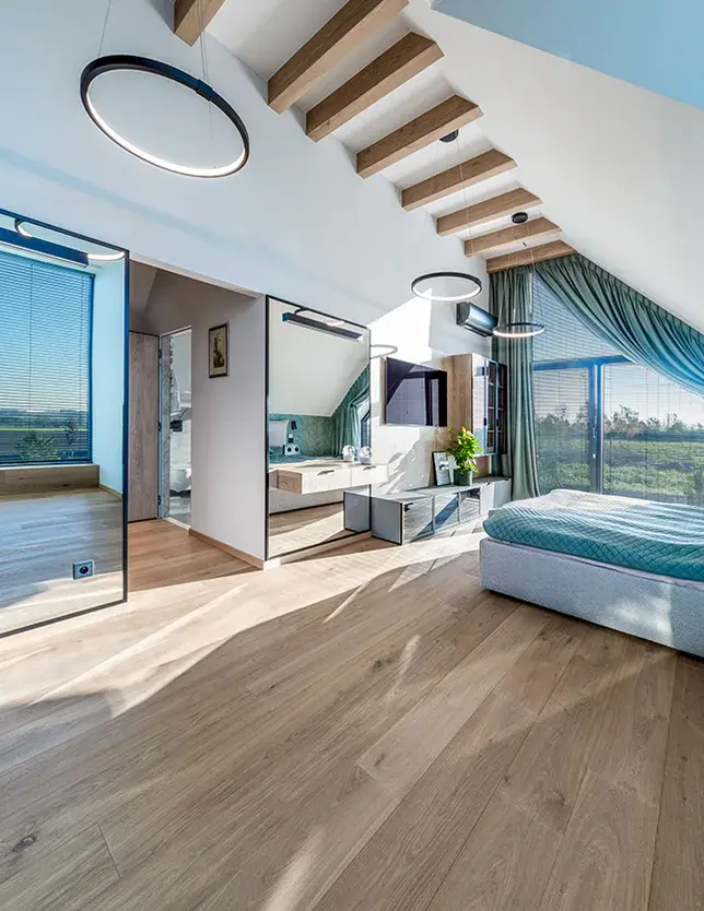 Designová podkrovní ložnice v domě Tyniec Mały s přiznanými dřevěnými trámy, kde velkorysá dubová prkna Oakcent Rustic v přírodním odstínu Pure a délce 2,2 metru opticky sjednocují prostor se šatnou a velkým zrcadlem.