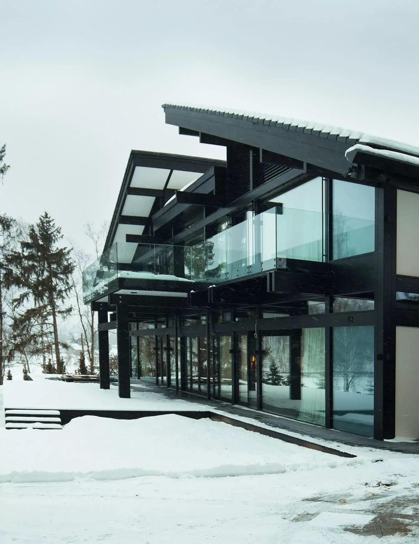 Exteriér moderní prosklené Vily Trnávka v zimní zasněžené krajině, kde černá dřevěná konstrukce stavby z kolekce Ink ladí s tmavými okenními rámy a velkorysými terasami se skleněným zábradlím.