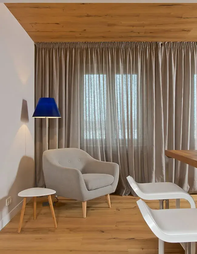 Interiér Valašského Apartmánu s dubovou podlahou Oakcent z kolekce Honey položenou ve vzoru rybí kost (Herringbone), která doplňuje barevný sedací nábytek, dřevěné dělící příčky a moderní vinotéku pod dekorativním zvlněným podhledem.