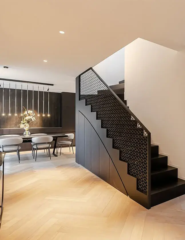 Interiér soukromého bytu Josefov s výrazným černým schodištěm z kolekce Ink, které je doplněno o geometrické perforované zábradlí a tvoří moderní dominantu nad světlou dubovou podlahou položenou ve vzoru rybí kost.